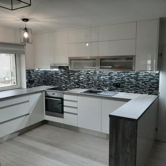 Kuchyňská linka v rodinném domě do tvaru G s barovým pultem a protilinkou v dekoru vysoký lesk.Jako obklad kuchyňské linky byla použita skleněná mozaika.