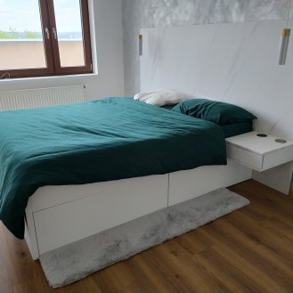 Manželská postel na míru s úložným prostorem v dekoru Levanto bílý a šatní skříň na míru s lakovanými pojezdovými dveřmi černé barvy.