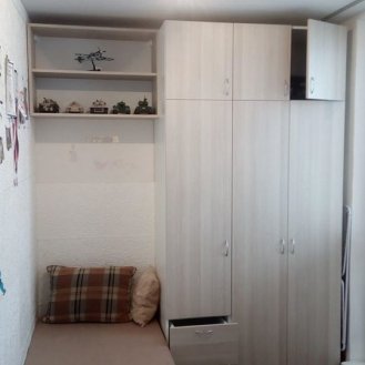 Šatní skříň a poličky umístěné v malém studentském pokojíku.